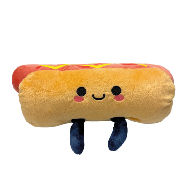 The 2025 Hotdog Plush is a smiling hot dog toy with rosy cheeks, black eyes, two navy blue legs, and a yellow squiggle on top like mustard.
